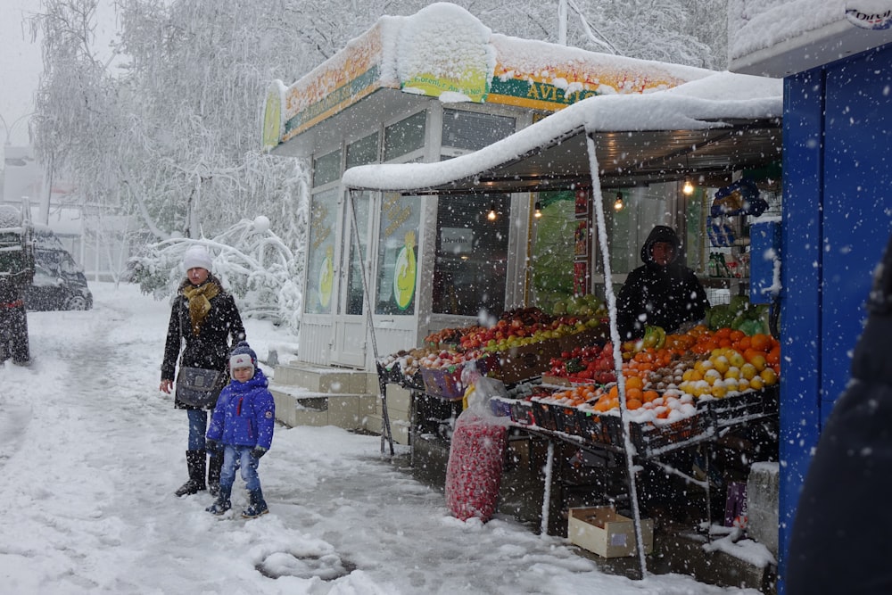 woman and child walking near store on snowy field during daytime