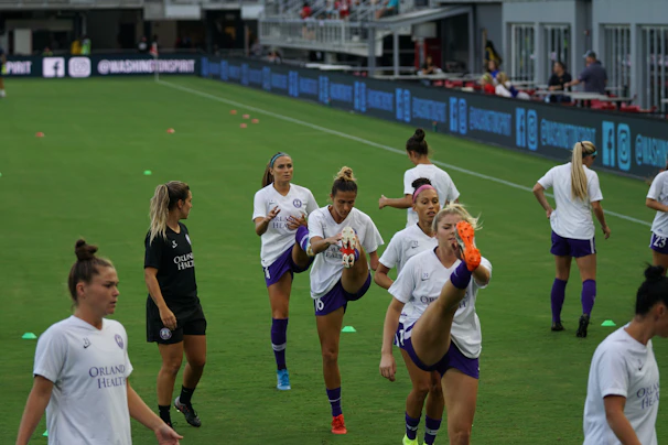 Coach demonstrating proper stretching techniques to a focused group of campers on a grassy field.