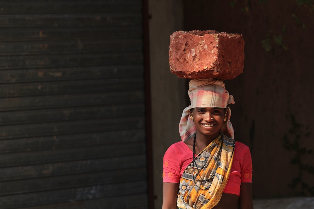 smiling woman carrying brown stone on head