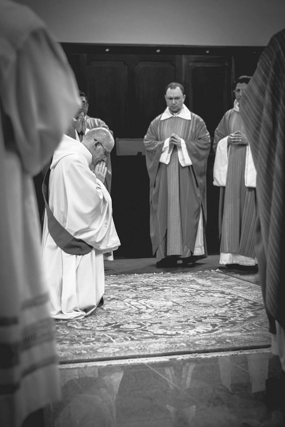 grayscale photo of priest kneeling on carpet