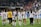 A group of female soccer players in matching uniforms, with numbers and names on their backs, walk together on a soccer field. They appear to be leaving the field, and some are holding or interacting with a child. The background shows a stadium with a crowd of spectators.