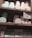 A set of wooden shelves displays various tins and boxes of champagne truffles and chocolate tiles. The truffles are stored in round tins of pastel colors, including mint green and light pink. Below, rectangular boxes labeled as chocolate tiles are also neatly arranged. A small sign is present, offering details about a 'Sweetness Rewards' program.
