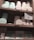 A set of wooden shelves displays various tins and boxes of champagne truffles and chocolate tiles. The truffles are stored in round tins of pastel colors, including mint green and light pink. Below, rectangular boxes labeled as chocolate tiles are also neatly arranged. A small sign is present, offering details about a 'Sweetness Rewards' program.