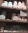 A set of wooden shelves displays various tins and boxes of champagne truffles and chocolate tiles. The truffles are stored in round tins of pastel colors, including mint green and light pink. Below, rectangular boxes labeled as chocolate tiles are also neatly arranged. A small sign is present, offering details about a 'Sweetness Rewards' program.