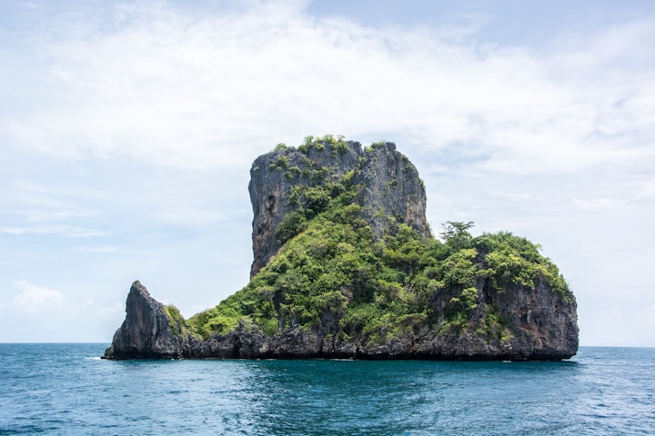 Large rocky island covered in green foliage in the middle of a calm sea on a bright sunny day