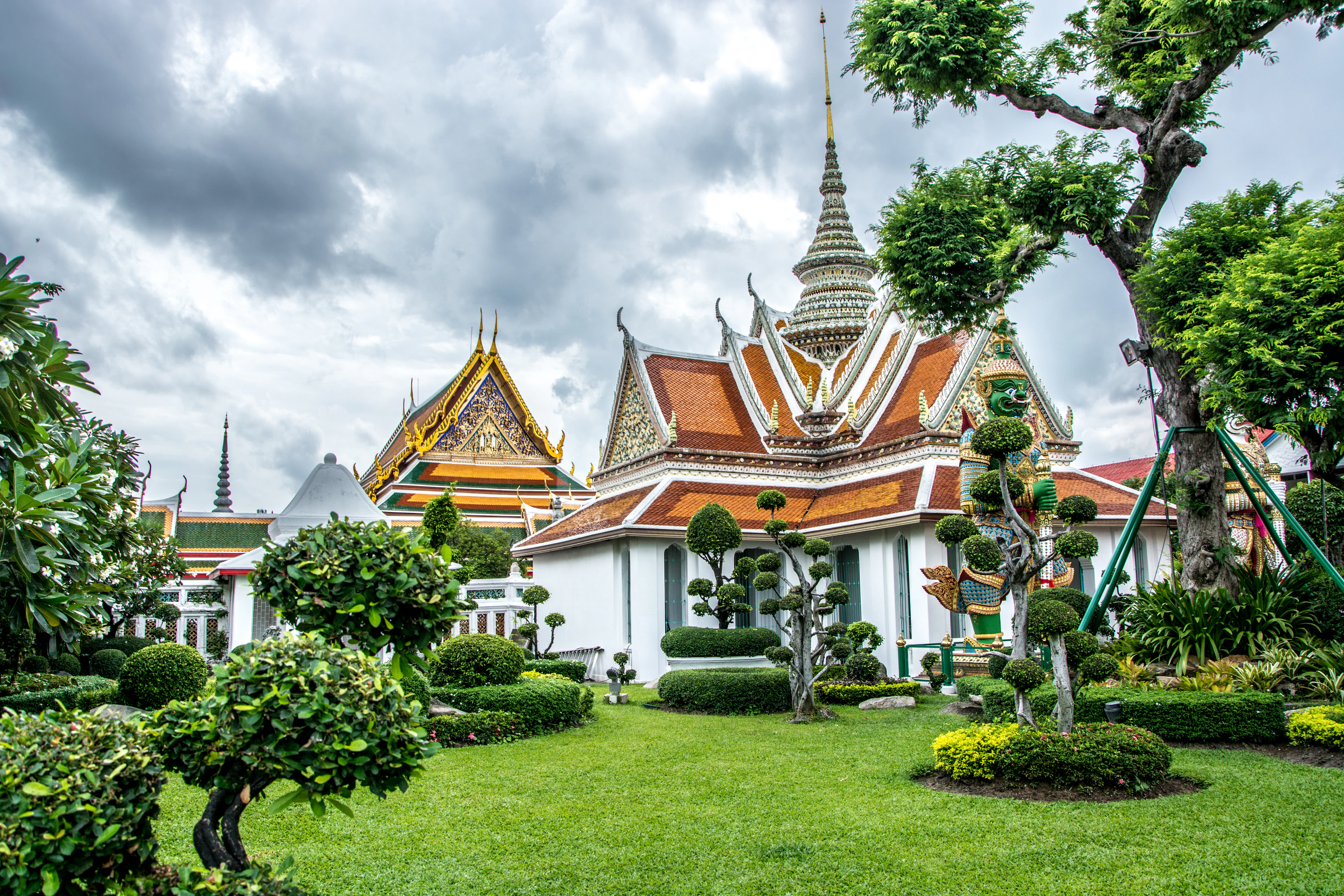 Gilded temple roofs and white prangs above clipped lawns in a Bangkok temple compound
