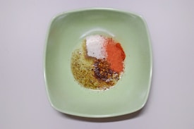 A square green plate containing a variety of spices, including chili powder, salt, and crushed pepper flakes, arranged in a pile.