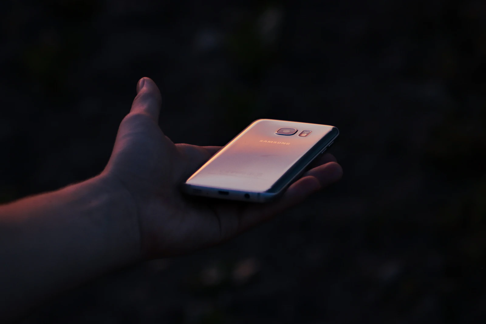 Open hand holding a smartphone at dusk with warm light reflecting off the screen