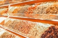 A vibrant display of various dried herbs and spices arranged in transparent containers on angled shelves. The collection includes an assortment of colors and textures from different varieties of dried produce.