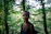 A smiling woman standing in a lush forest, holding a map and wearing eco-friendly travel gear.