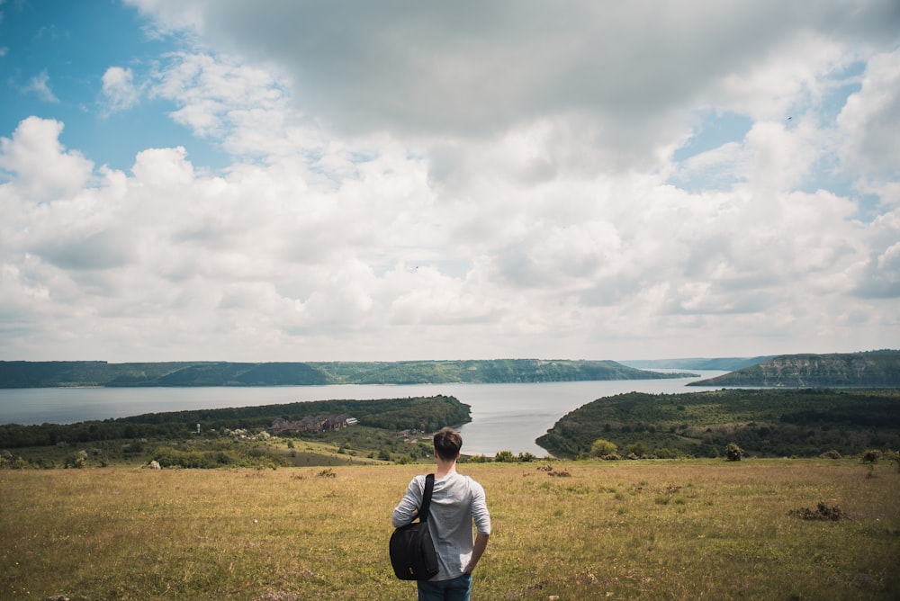 man wearing white shirt with black bag standing in front of body of water during daytime