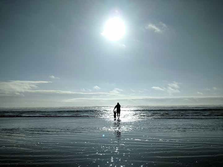 The sun shining on a beach with a man and a small child playing with only their silhouettes being visible