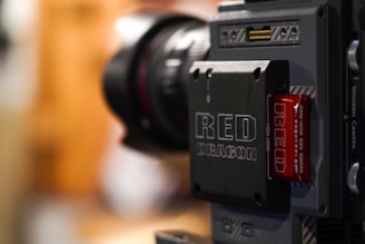 Close-up of a RED digital cinema camera showing the details of its components, including a lens and a module labeled RED DRAGON. The camera appears sophisticated and compact.