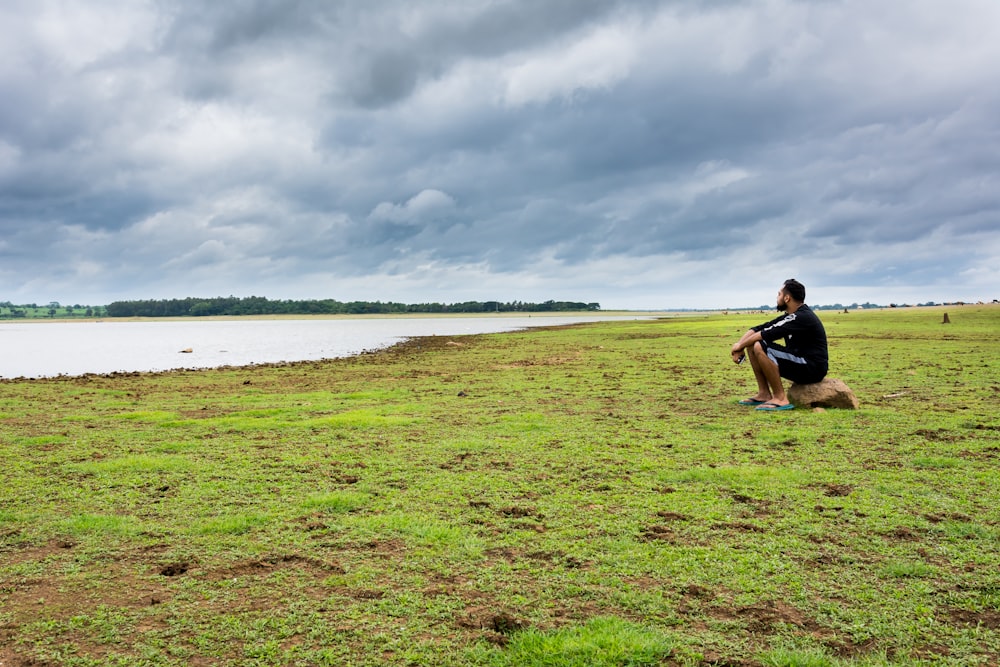 person sitting on green grass under cloudy sky during daytime