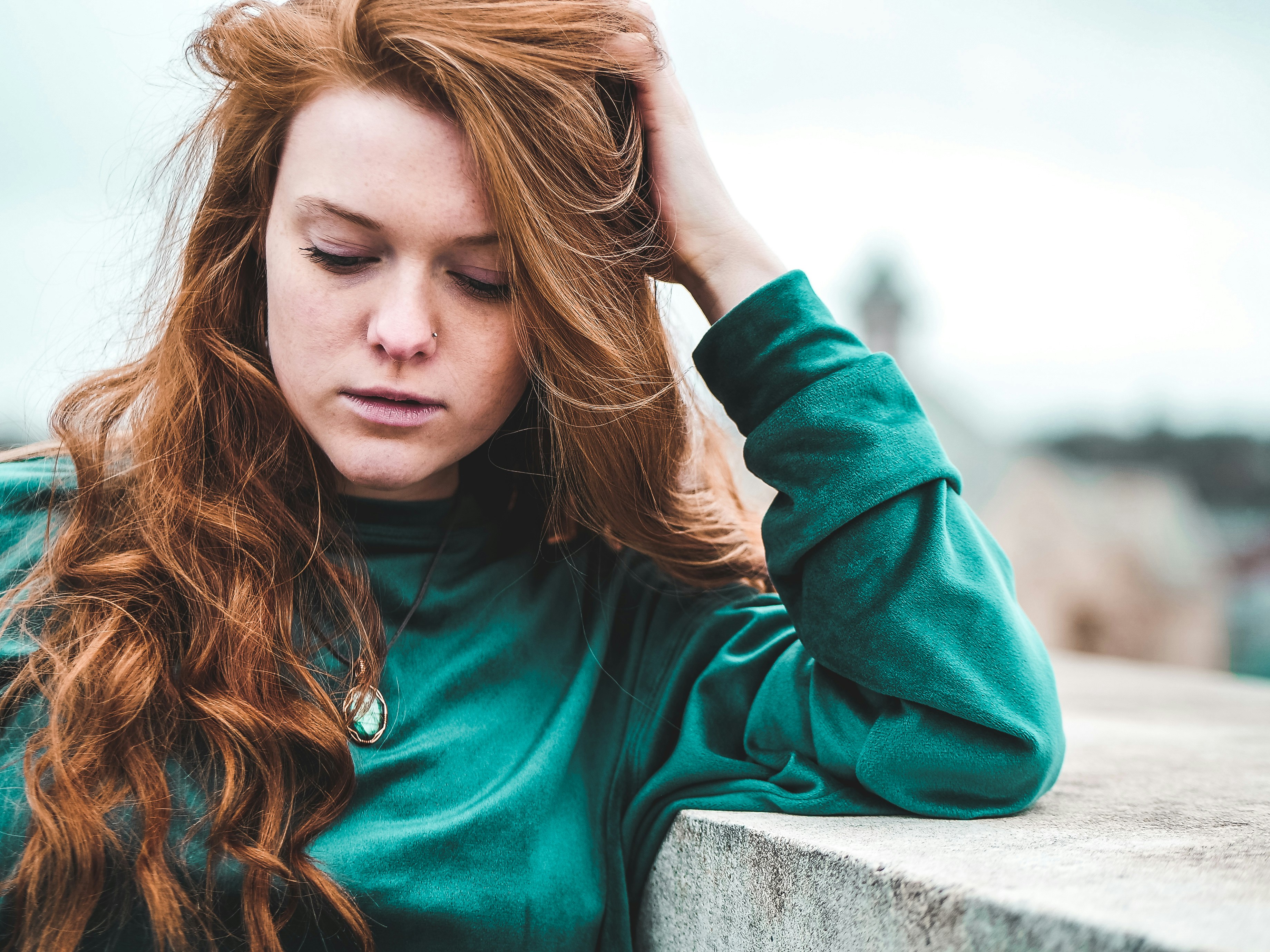selective focus photography of woman wearing green long-sleeved top leaning on wall