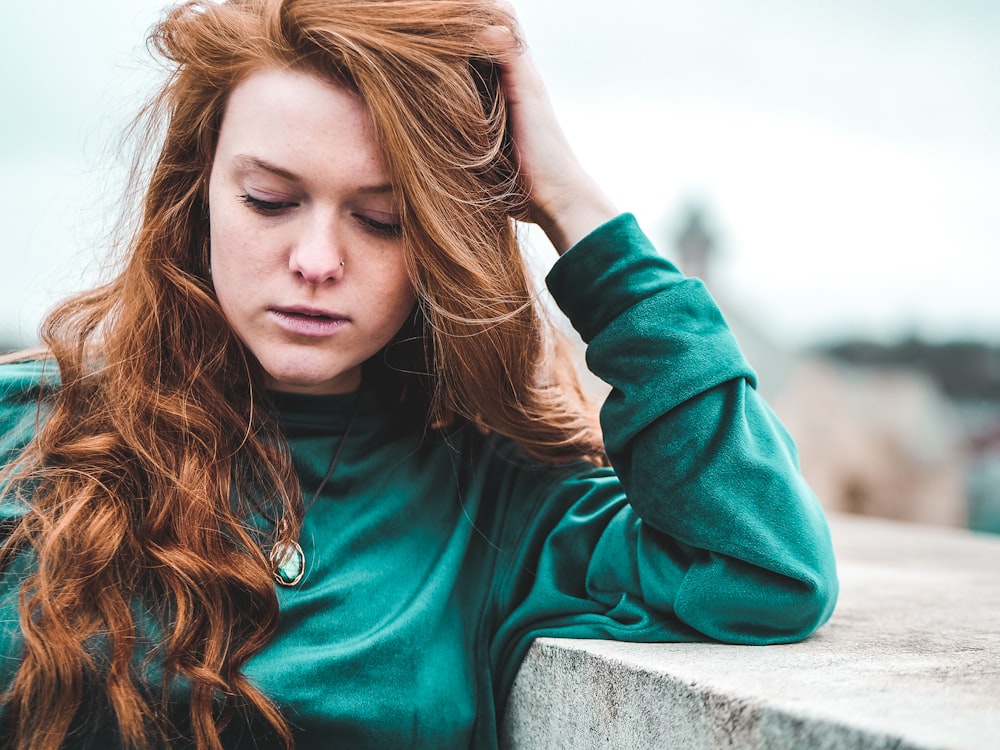 selective focus photography of woman wearing green long-sleeved top leaning on wall