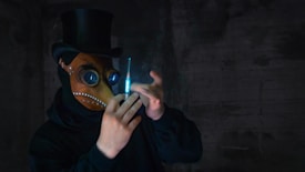 A person wearing a dark outfit and a plague doctor mask with a top hat is holding a glowing syringe. The background is dark and eerie, giving a mysterious and unsettling atmosphere.