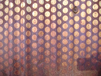 The image features a close-up view of a metallic surface covered with a pattern of evenly spaced circular rust spots. The surface appears textured with a combination of rusty orange and brown tones, suggesting oxidation.