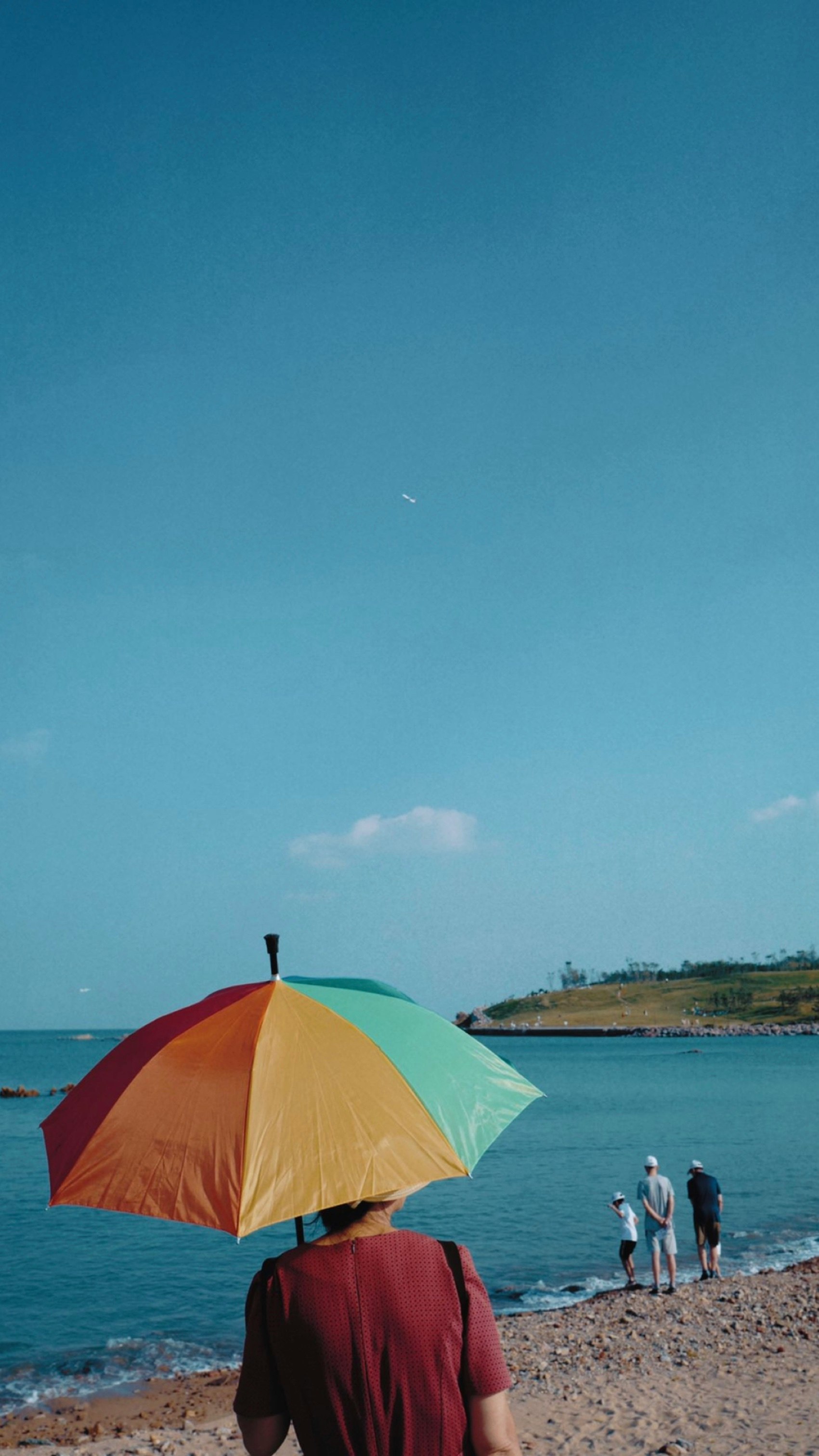 person holding multicolored umbrella in front of body of water