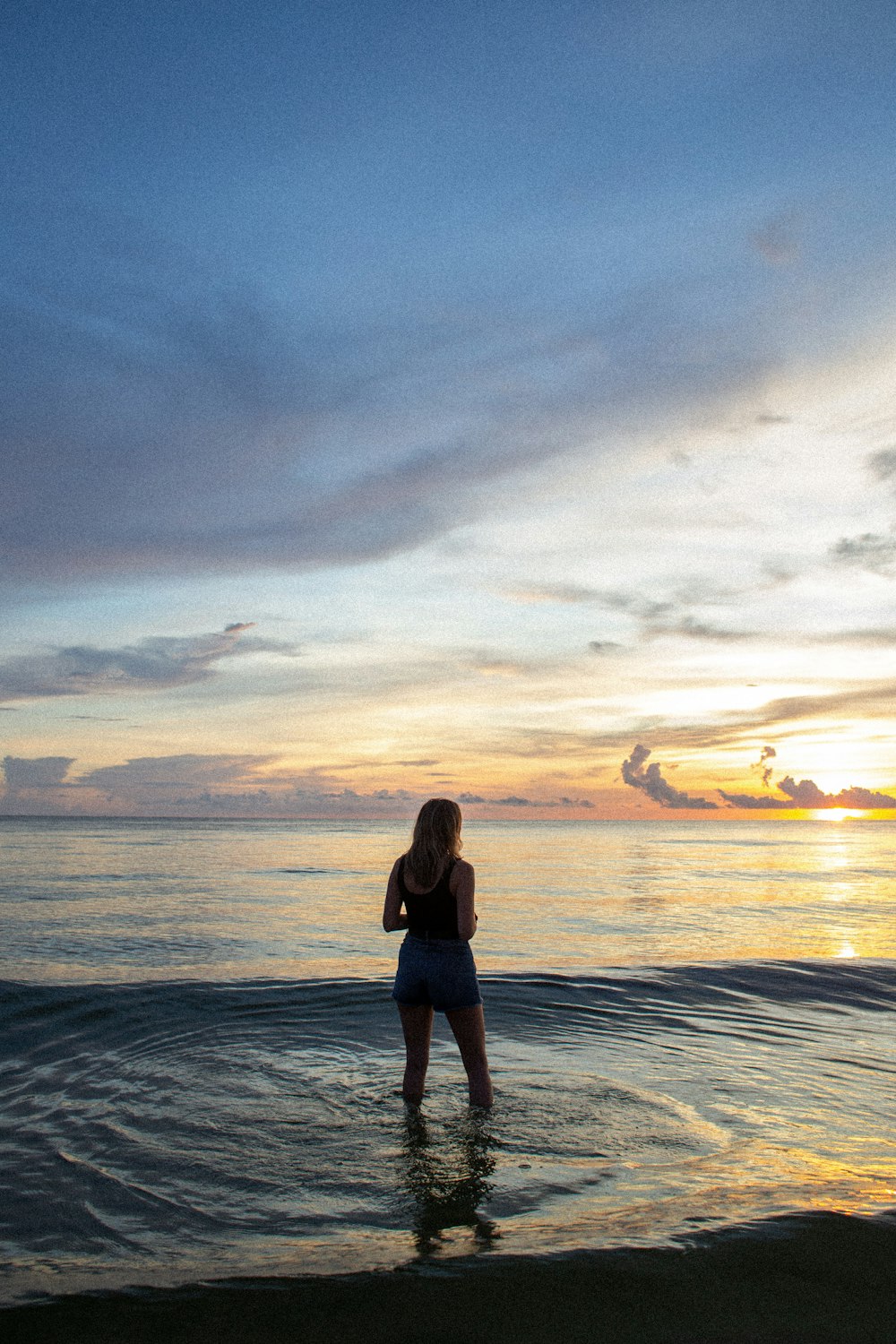 woman wearing black tank top and blue denim short standing on seashore