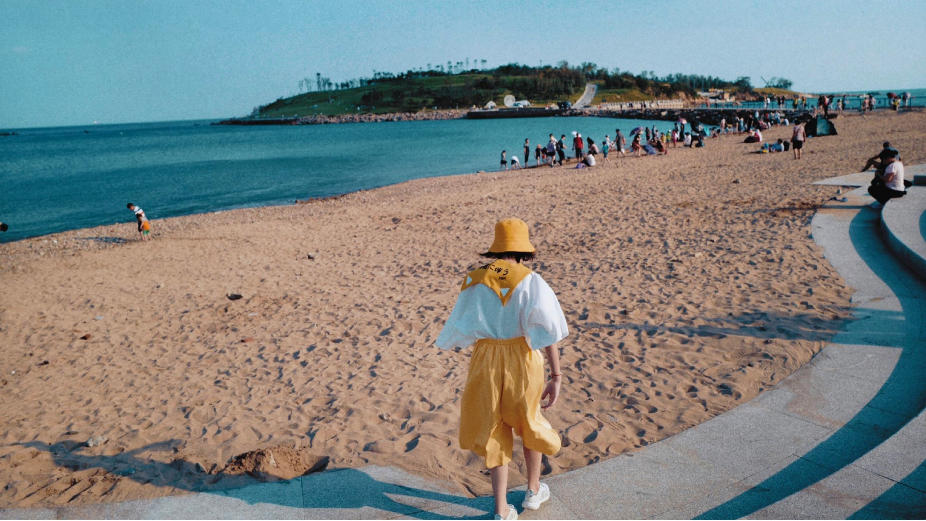 woman wearing yellow hat walking besides seashore