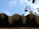 A close-up view of a wavy metal roof edge against a bright blue sky. In the background, blurred green leaves partially visible, adding a natural contrast.
