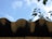 A close-up view of a wavy metal roof edge against a bright blue sky. In the background, blurred green leaves partially visible, adding a natural contrast.
