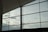 Large glass windows reveal a cloudy sky, with soft light filtering through. The metal frames create a geometric pattern against the sky, capturing a modern architectural element.