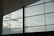Large glass windows reveal a cloudy sky, with soft light filtering through. The metal frames create a geometric pattern against the sky, capturing a modern architectural element.