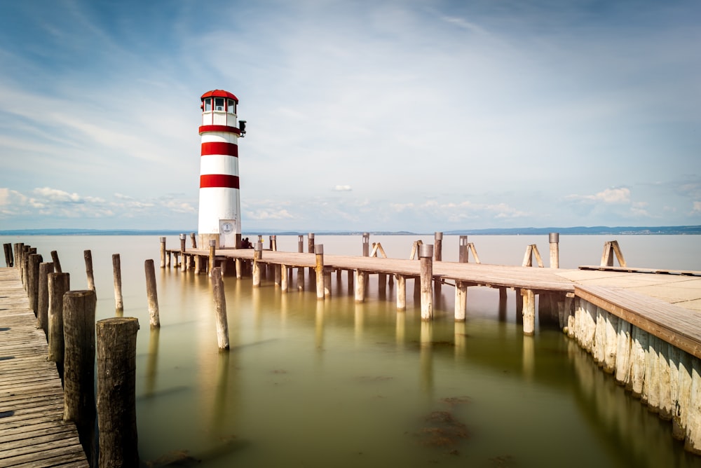 white and red lighthouse beside wooden dock