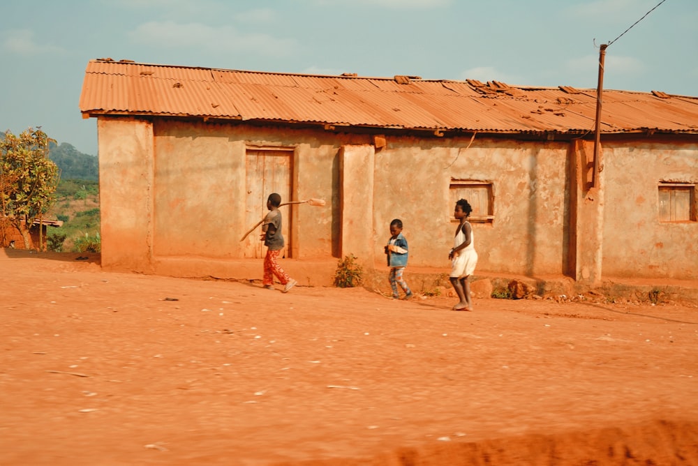 three kids standing beside concrete building