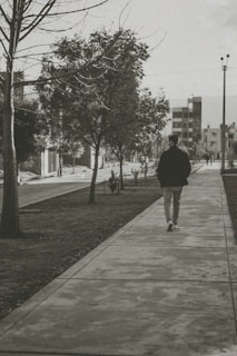A quiet black-and-white street scene showing a lone figure walking past old buildings.