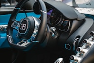 A close-up view of a luxury car's interior, featuring a steering wheel with a prominent logo, a sleek dashboard with a speedometer, and various metallic control knobs. The interior design includes high-quality materials, such as leather and carbon fiber.