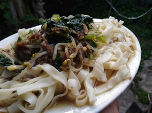 Close-up of a delicious ketoprak plate with soft lontong, fried tofu, fresh bean sprouts, vermicelli, crackers, and thick peanut sauce.