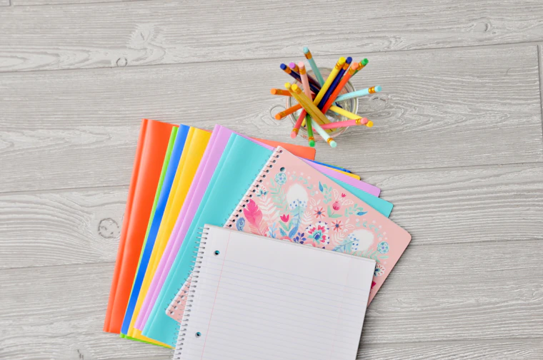 Cuadernos de colores apilados junto a un vaso lleno de lápices