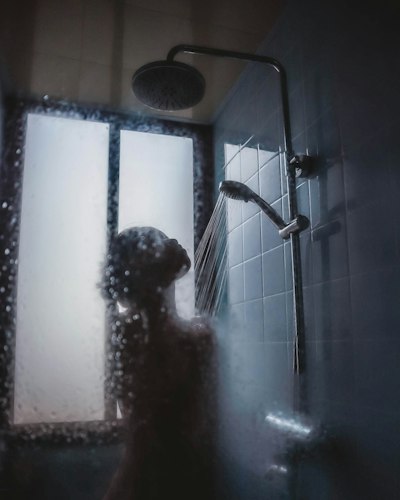 A person standing calmly under running water with eyes closed
