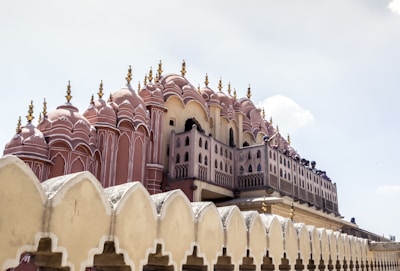 An ornate, pink sandstone facade with numerous small windows and decorative spires. The architecture reflects a blend of traditional design and artistic flourishes, characteristic of a historic palace or landmark.