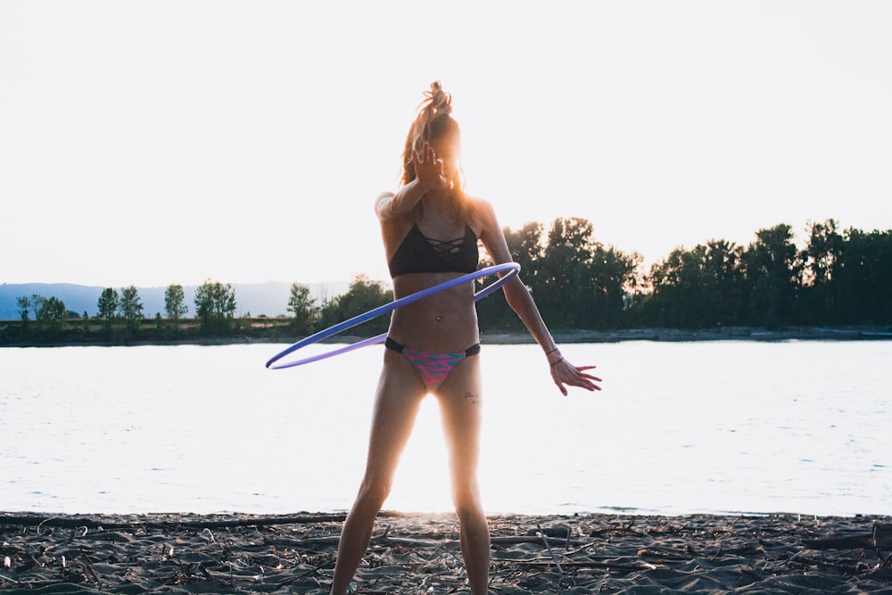 Mulher de biquíni usando Hoola Hoop pela costa durante a hora dourada