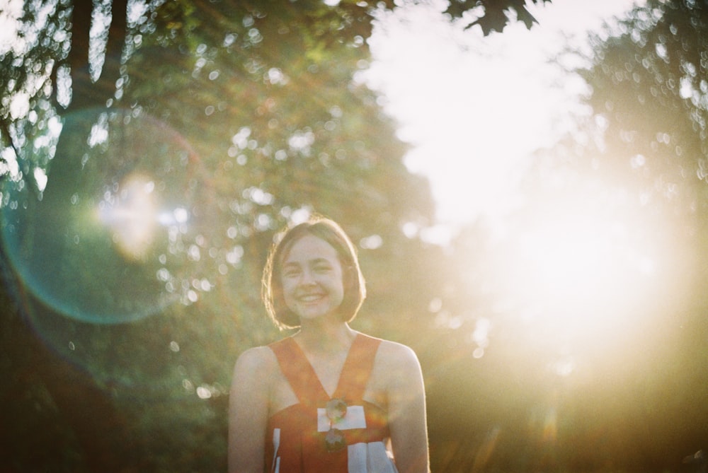 sun rays coming through woman wearing orange sleeveless top standing and laughing during daytime