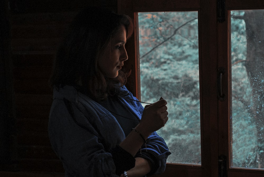 woman wearing blue long-sleeved shirt standing and staring on window