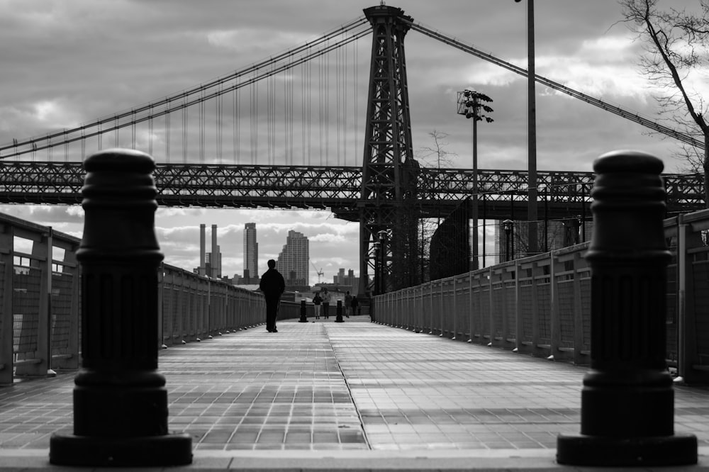 grayscale photo of person walking near bridge