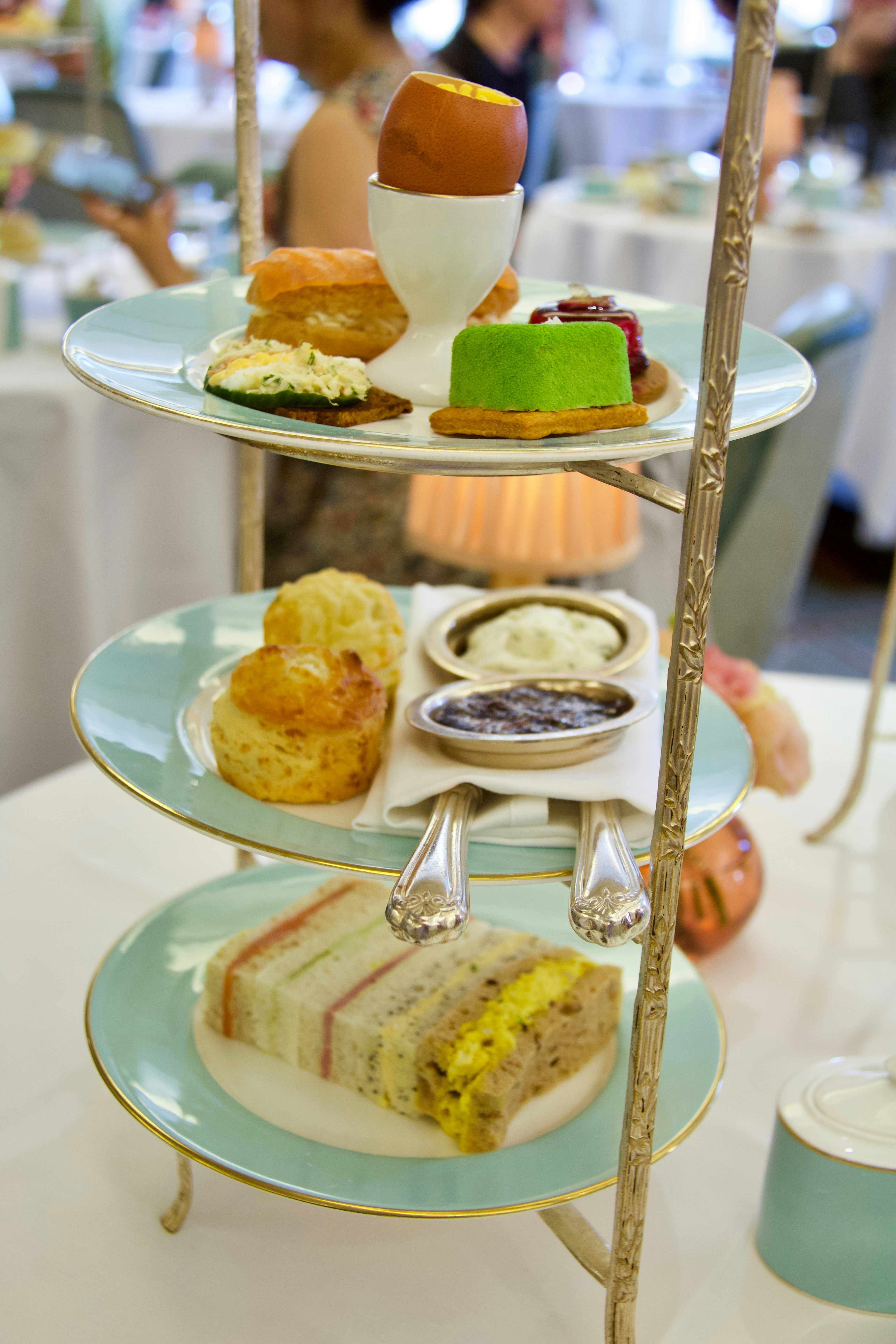 Three-tier afternoon tea stand with finger sandwiches, scones and mini cakes on white tablecloth, elegant tea room