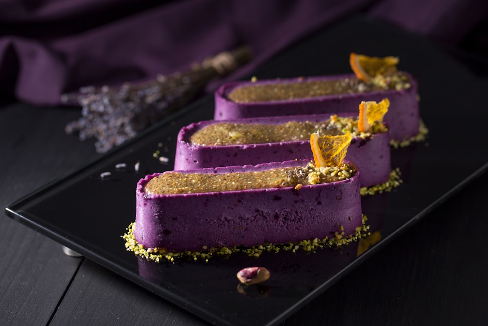 a black plate topped with three purple desserts