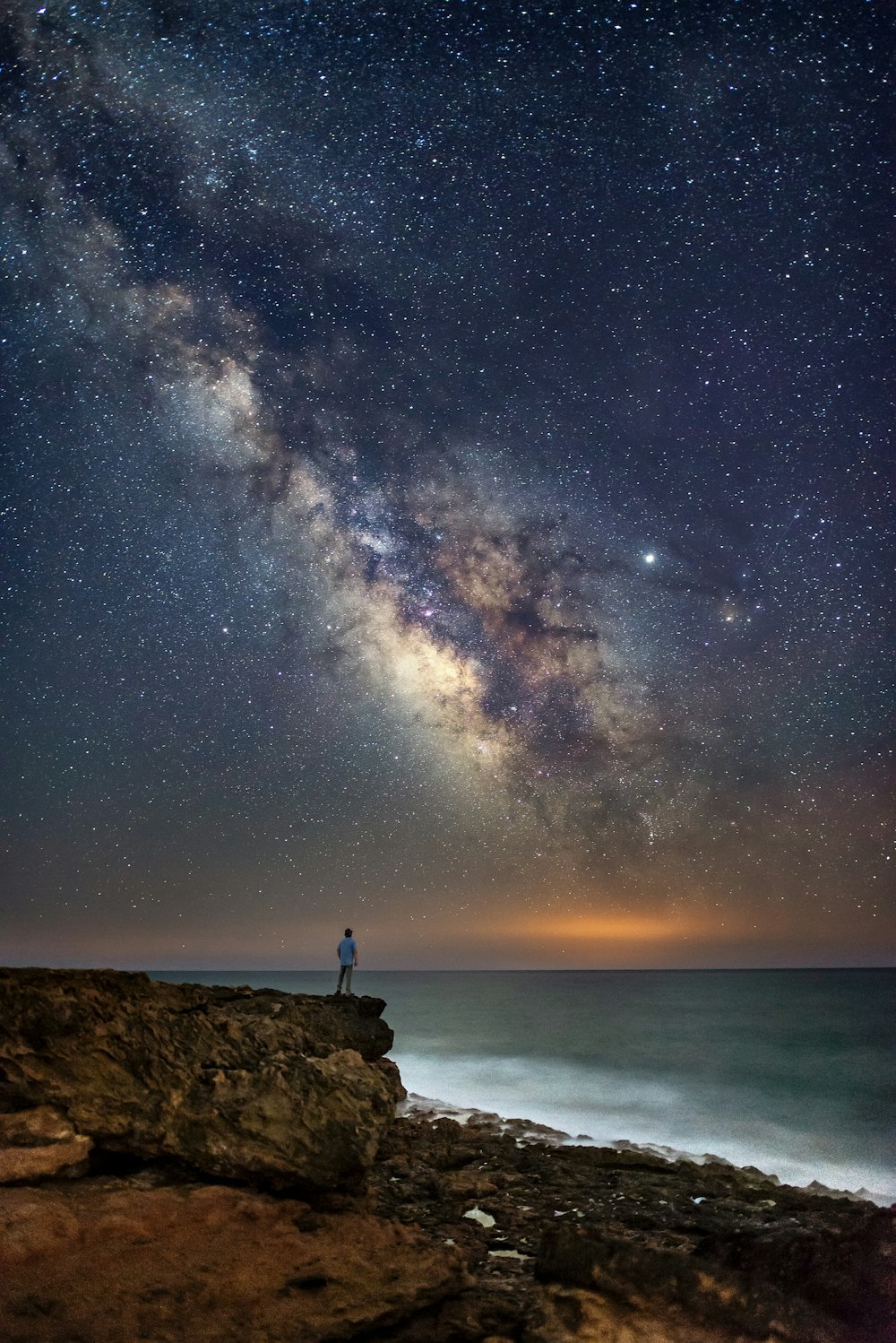 Persona in piedi sulla scogliera durante la notte