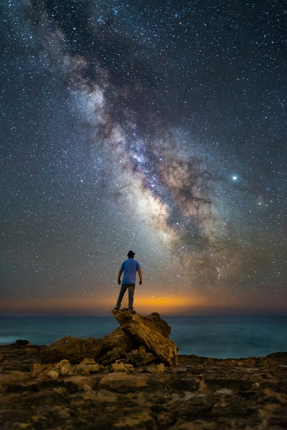 Mann steht auf Felsen mit Blick auf den Ozean unter Sternennacht
