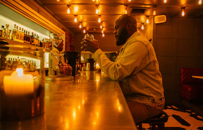 A cozy, dimly lit bar corner with glowing red and gold lights reflecting off glassware and bottles.
