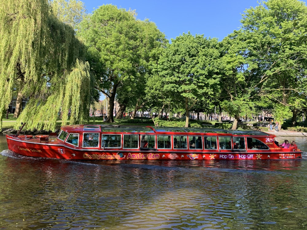 red passenger boat beside green leafed trees