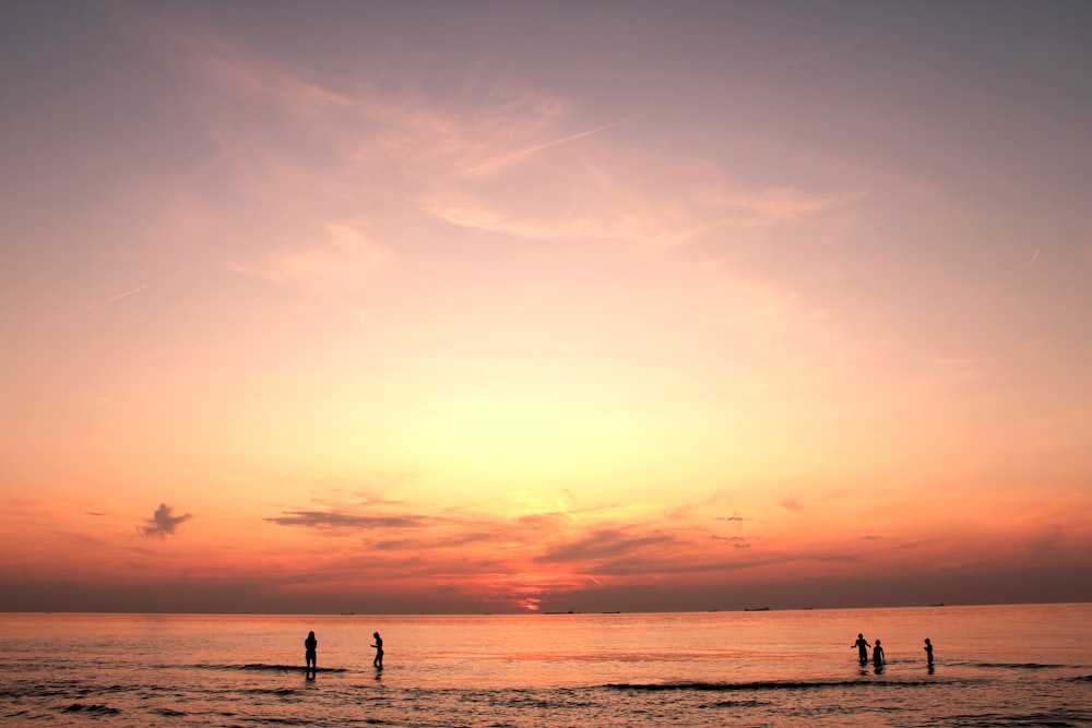 Silhouette von Menschen, die während der goldenen Stunde am Meeresufer stehen