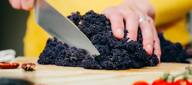 person slicing a black-leafed vegetable