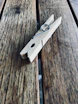 A wooden clothespin rests on a textured wooden surface, showcasing its simple metal spring mechanism. The wood has a natural finish with visible grain patterns, adding a rustic feel.